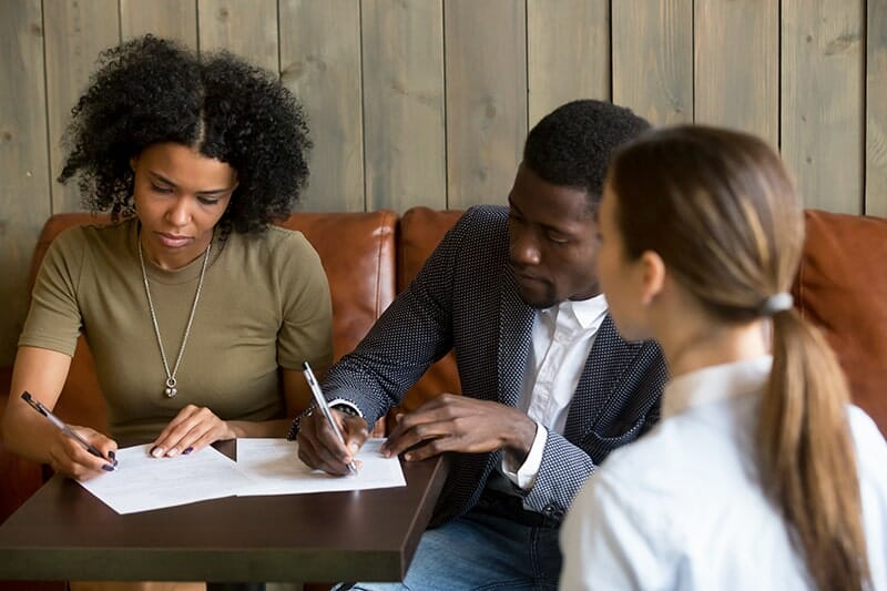 a couple sitting at a table and signing the closing papers for their house