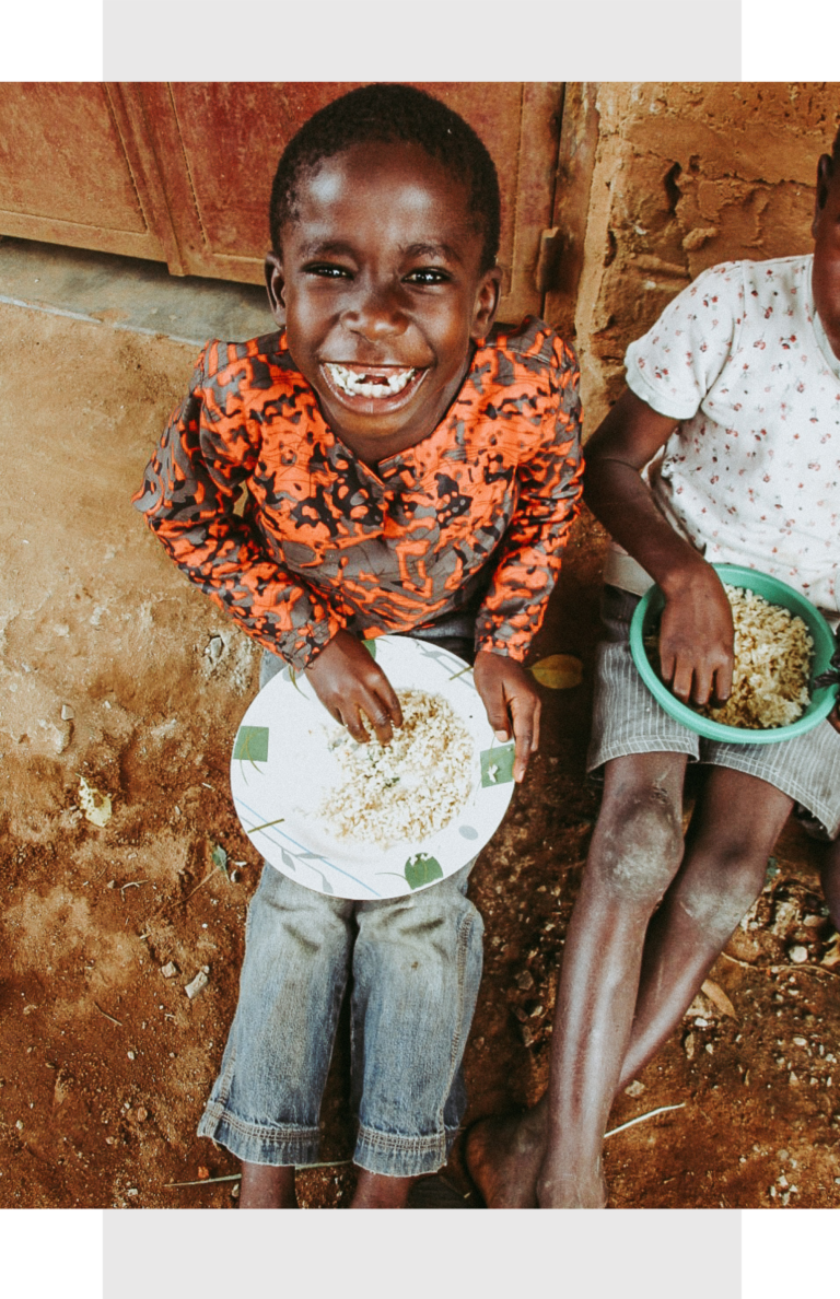 a smiling african child eating rice from a bowl with his fingers
